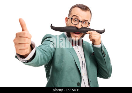 Excited young man holding fake moustache on his face and giving a thumb up isolated on white background Stock Photo