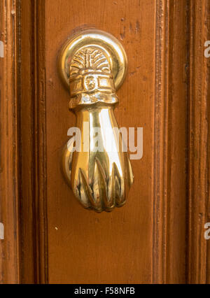 Front view of brass door knocker shaped like a hand on old wooden door Stock Photo