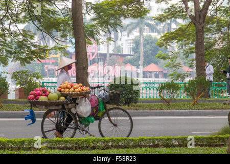 Vietnamese street vendor with her bicycle loaded with fruit, walking through Hanoi,Vietnam Stock Photo