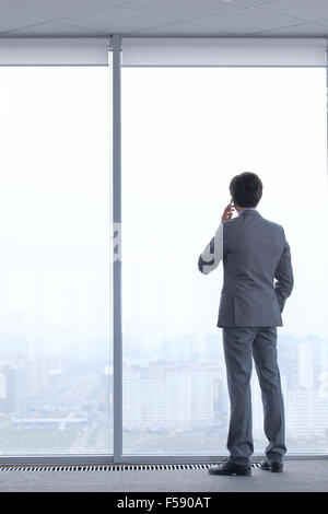 Businessman standing near window, looking at city and talking by phone Stock Photo