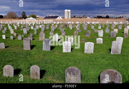 Lancaster County, Pennsylvania:  Simple stone grave markers in an Amish burial ground with farm silos in the distance Stock Photo