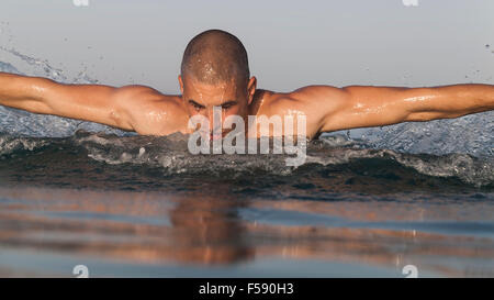 Muscular young man swimming butterfly in sea water Stock Photo