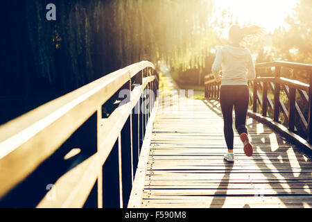 Beautiful female jogger running during sunset across bridge Stock Photo