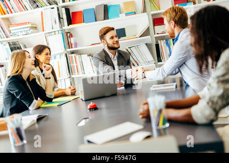 Businesspeople shaking hands in office with coworkers and staff sitting at the table with them Stock Photo