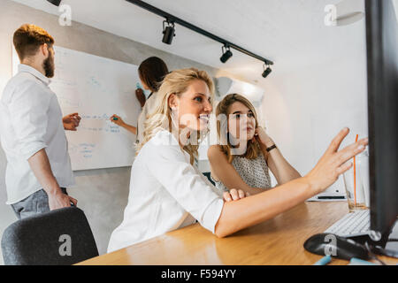 Coworkers in office pointing at desktop and discussing contents displayed on monitor Stock Photo