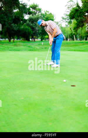 Golfer takes the putting green shot and ball is closing in on the hole Stock Photo