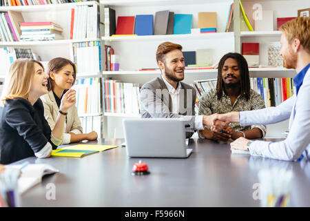 Businesspeople shaking hands in office with coworkers and staff sitting at the table with them Stock Photo