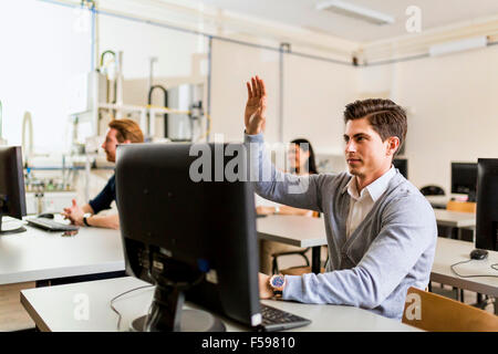 Young handsome man sitting in front of a pc raising hand Stock Photo
