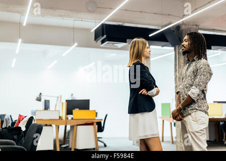 Colleagues talking in office and smiling while standing Stock Photo