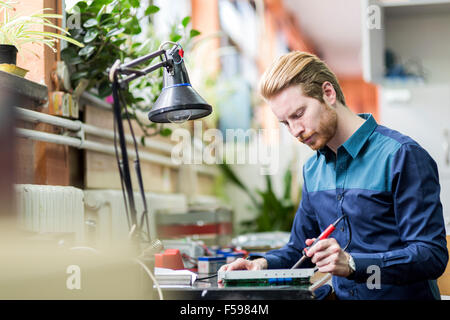 Young handsome man soldering a circuit board and working on fixing hardware Stock Photo