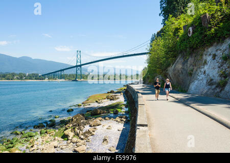 Young couple walk along the Stanley Park Seawall with Lions Gate Bridge (1938) and the North Shore in the background, Vancouver, Canada Stock Photo