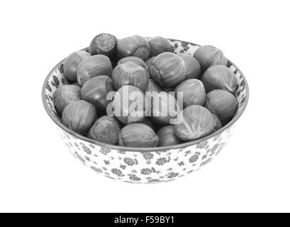 Hazelnuts in shells, in a porcelain bowl with a floral design, isolated on a white background - monochrome processing Stock Photo