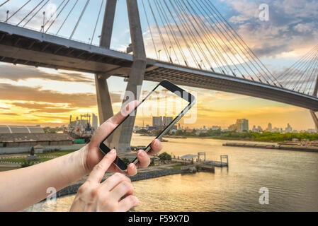 female hand hold and touch screen smart phone, on bridge blurred background. Stock Photo