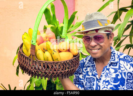 Portrait of a smiling Filipino man wearing a fedora hat, sunglasses and a flower shirt holding a basket of fresh fruit. Stock Photo
