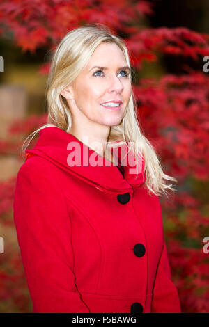 portrait of blond woman in a red coat in front of a tree in autumn Stock Photo