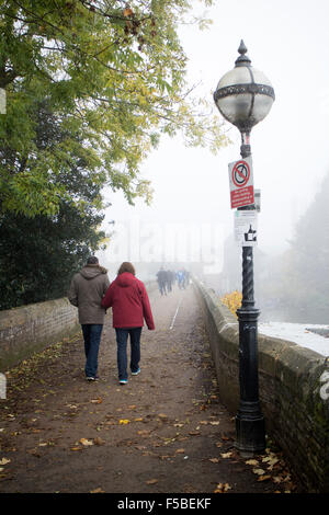 Stratford-upon-Avon, Warwickshire, UK. 1st November, 2015. Fog envelops the town of Stratford-upon-Avon on the first day of the month. People take a morning stroll across the Tramway Bridge over the River Avon. Credit:  Colin Underhill/Alamy Live News Stock Photo