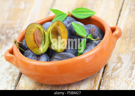 Juicy plums in clay bowl on rustic wooden surface
