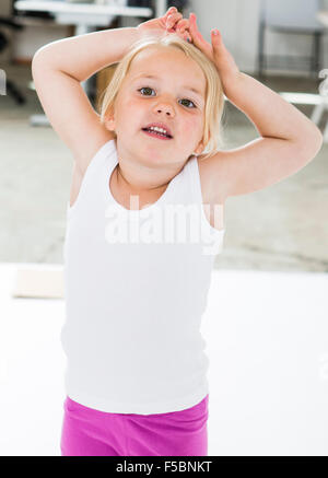 Four year old girl standing with her hands and arms above her head, looking into the camera. Stock Photo