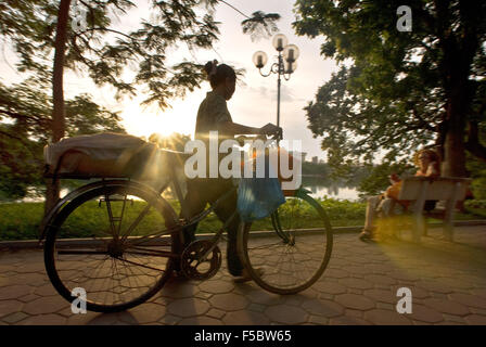 Hoan Kiem Lake Hanoi, Vietnam, overhanging flame of the forest trees, benches. Hanoi. Vietnam. Sunset and man with a bicycle. Pe Stock Photo