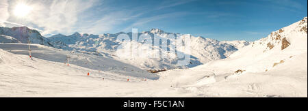 View down a snowy piste with skiers and mountain valley Stock Photo