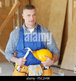 Handyman with hammer and protective helmet in house under construction Stock Photo
