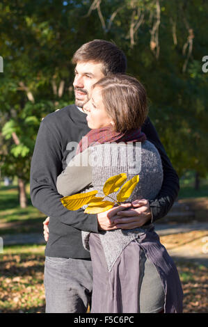 Happy loving couple hugging in the park while holding yellow autumn leaves Stock Photo