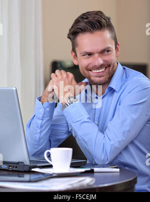 Young businessman laughing at home with a laptop and coffee Stock Photo