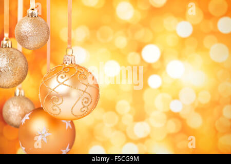Golden Christmas baubles hanging in front of defocused golden lights. Stock Photo