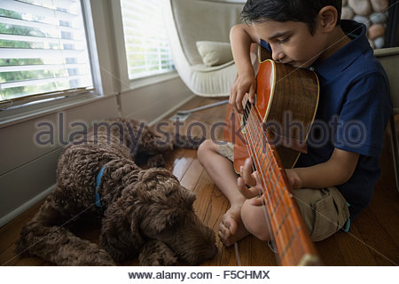 Dog sleeping next to boy playing guitar