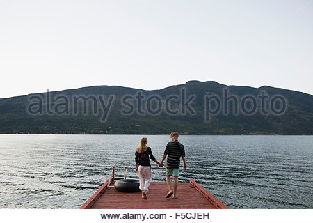 Young couple holding hands walking on lake dock