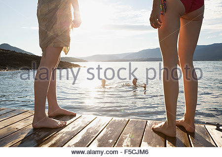 Women on dock watching men swimming in lake