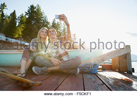 Smiling young couple taking selfie dock near canoe