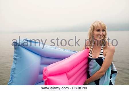 Smiling woman carrying pool rafts in lake