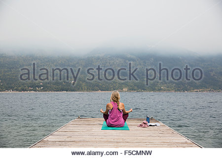 Mature woman lotus position yoga mat overlooking lake