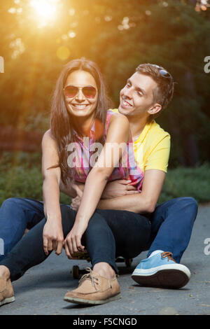 Young happy couple in love sitting on a skateboard outdoors Stock Photo