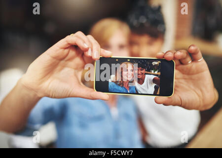 Two attractive young women friends taking a selfie on a mobile with the image displayed to the camera on the screen, young multi