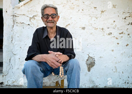 A man relaxes on the sidewalk with his worry beads in the mountain village of Anogia, on the island of Crete in Greece Stock Photo