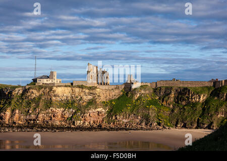 Castle, Abbey and Coastguard watch station on the cliffs at Tynemouth. A lone walker strolls on the sands in low evening light. Stock Photo