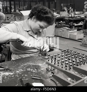 1950s historical, female factory worker using soldering machine tool at workbench. Stock Photo