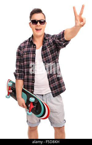 Vertical shot of a young male skater holding a skateboard and making a peace hand gesture isolated on white background Stock Photo