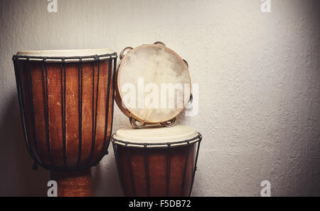 Various djembes and tambourine in front of a rustic wall. Stock Photo