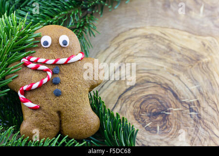 Gingerbread man with pine branches against background made of olive wood Stock Photo