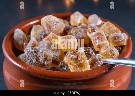 Macro of German Rock Sugar, brauner Kandis in a terracotta brown bowl and metal spoon. Close up. Stock Photo