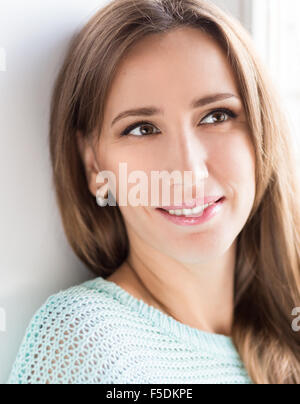 Close up portraite of thoughtful smiling girl. Young pretty caucasian woman in sweater near a window Stock Photo