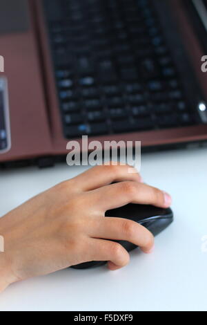 Hand holding computer mouse on white table with laptop in the background Stock Photo