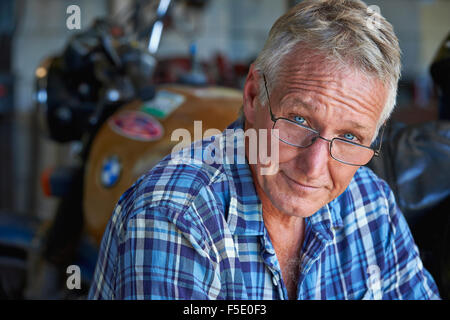 Portrait of a middle aged man and his old motor bike. His tough exterior is softened by his blue eyes and comforting smile. Stock Photo