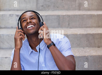Close up portrait of a smiling young man listening to music on headphones and looking up Stock Photo
