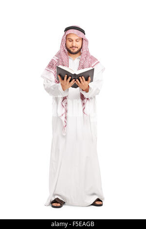 Full length portrait of a young male Arab in a white robe and a checkered veil reading a book isolated on white background Stock Photo