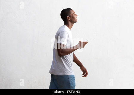 Side portrait of a cool black guy walking with cell phone against white wall Stock Photo