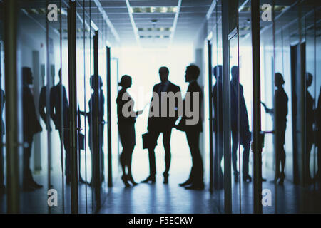 Blurred silhouettes of business people having meeting in corridor of office center Stock Photo